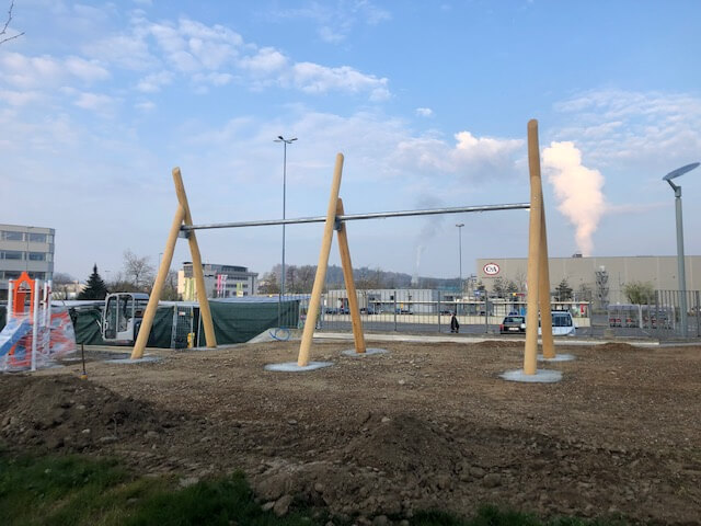 Un chantier de construction avec un grand échafaudage en bois sur un terrain nu devant un bâtiment industriel.