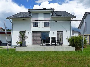 Zweistöckiges Einfamilienhaus mit moderner Terrasse, Garten und großer Fensterfront; ideale Wohnlage für Familien.