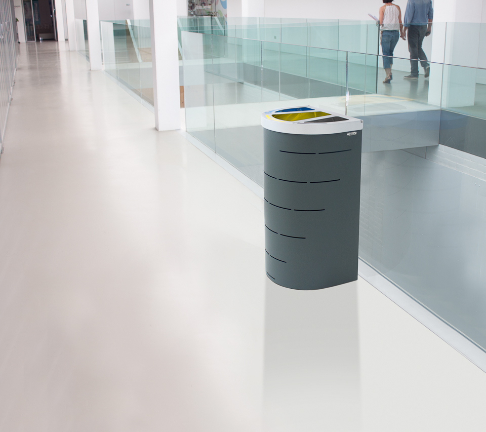 Ein moderner, stilvoller Mülleimer in einem hellen Bürogebäude neben einer Glasbalustrade.