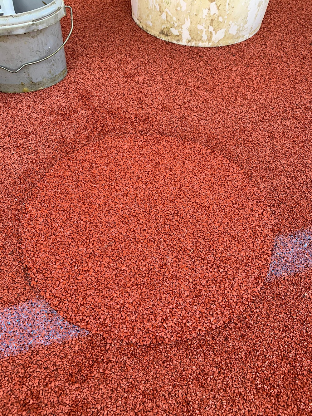 Gros plan sur un revêtement de sol en caoutchouc rouge en installation avec des seaux en arrière-plan