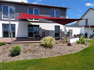 Une maison individuelle moderne avec une terrasse spacieuse ombragée par un voile d'ombrage rouge.