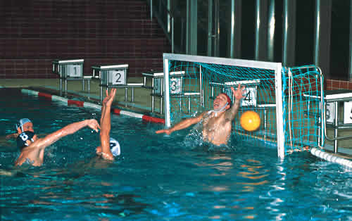 Ein spannendes Wasserballspiel in einem Hallenbad; ein Torwart versucht, einen Wurf zu blockieren.