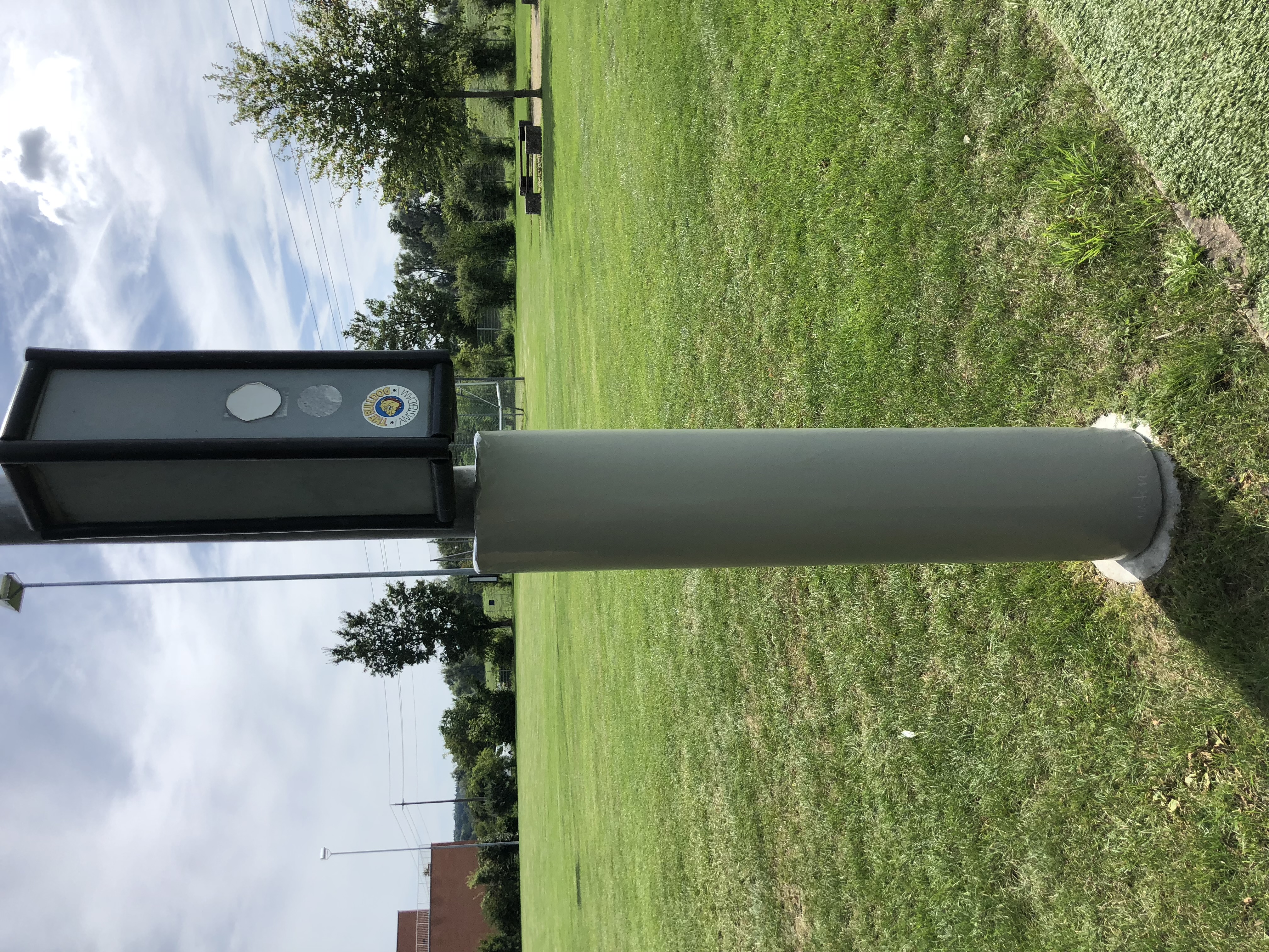 Eine graue Säule mit einem Schild auf einer großen, gepflegten Rasenfläche unter blauem Himmel